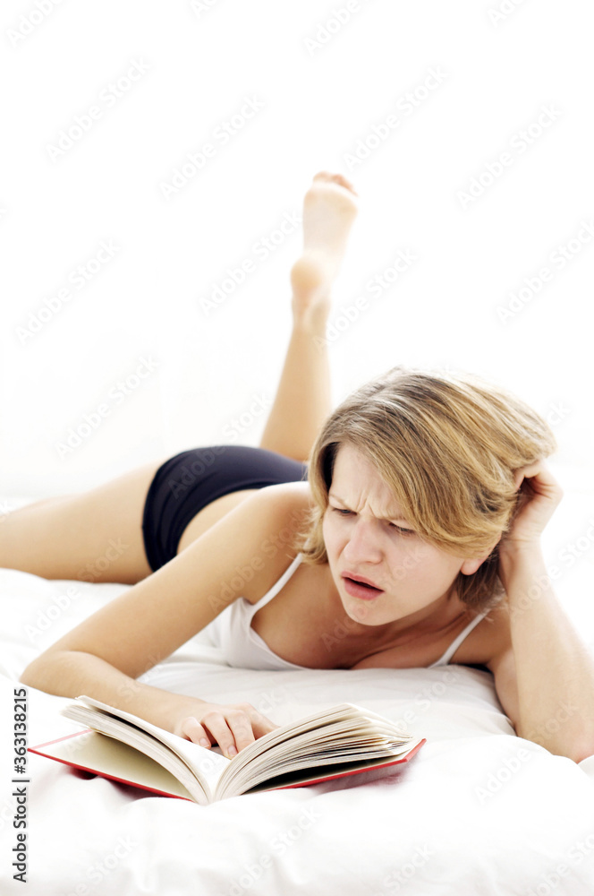 A woman lying on the bed scratching her head while reading A woman lying on the bed scratching her head while reading
