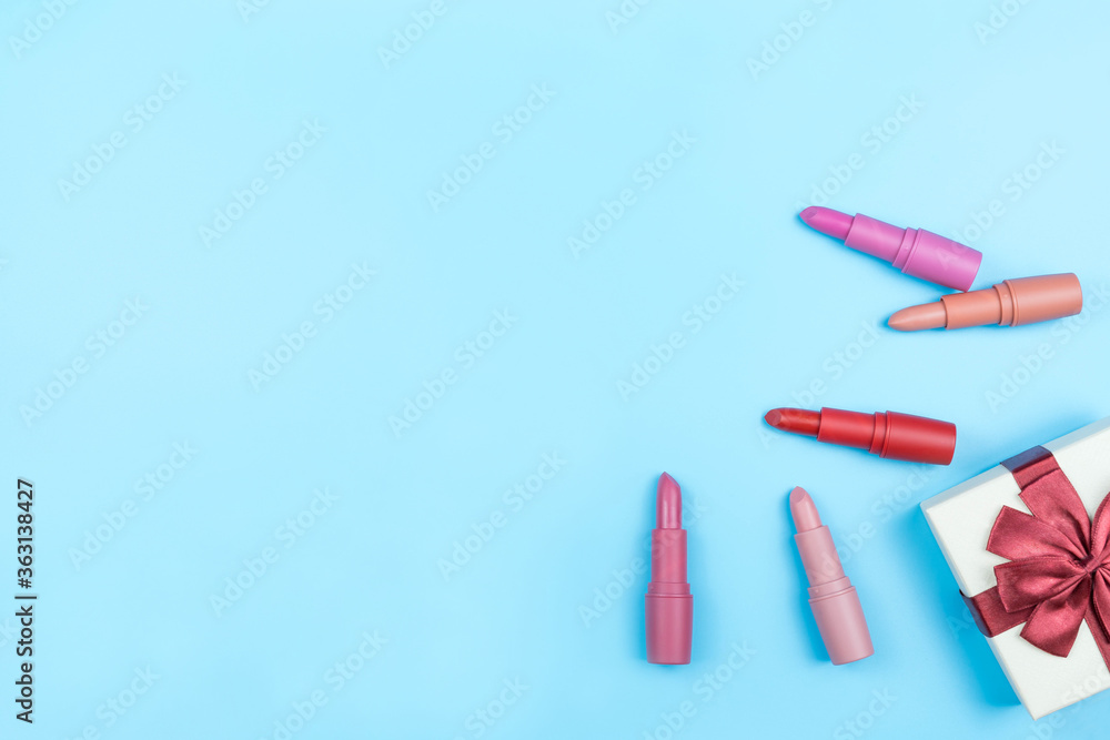 color lipsticks nude arranged on blue background with red ribbon tied gift box,copy space color lipsticks nude arranged on blue background with red ribbon tied gift box,copy space