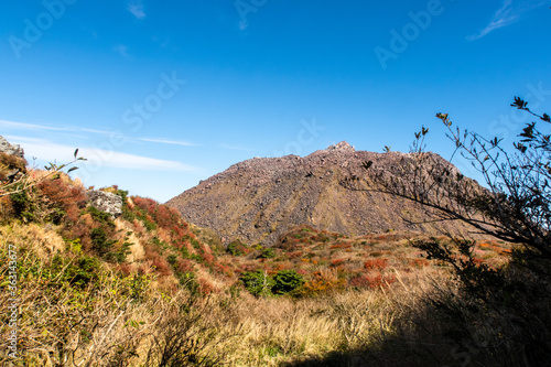 Picturesque autumn view of Unzen Nita Pass trail with rocky volcano peak, clear blue sky and colorful trees in Unzen-Amakusa National Park, Shimabara Peninsula, Nagasaki Prefecture, Japan.  photo