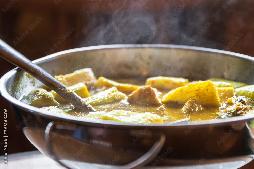 Yellow curry with fish and green taro (aaw dip) in hot pot on wooden table. Southern delicious food of Thailand. Yellow curry with fish and green taro (aaw dip) in hot pot on wooden table. Southern delicious food of Thailand.