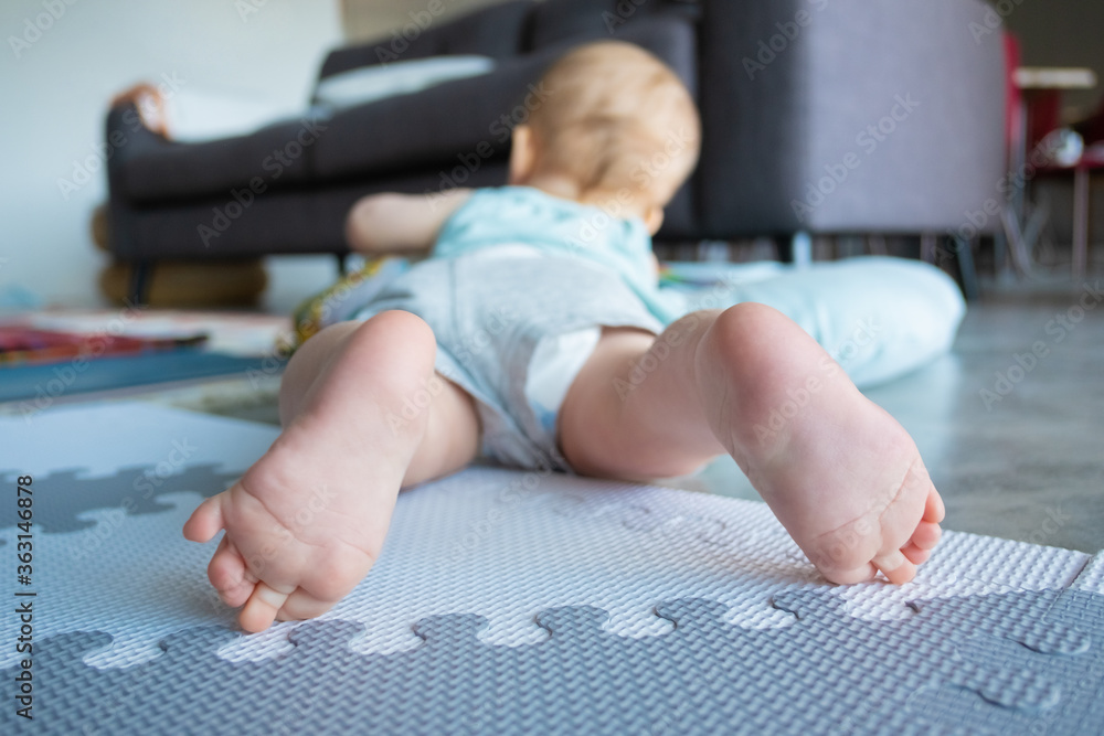 Closeup view of small baby legs or feet. Cute adorable infant lying on belly and playing on soft floor at home. Childhood and infancy concept - obrazy, fototapety, plakaty 