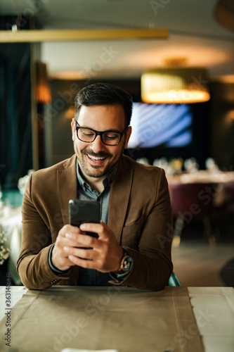 Happy man using smart phone at restaurant, portrait.