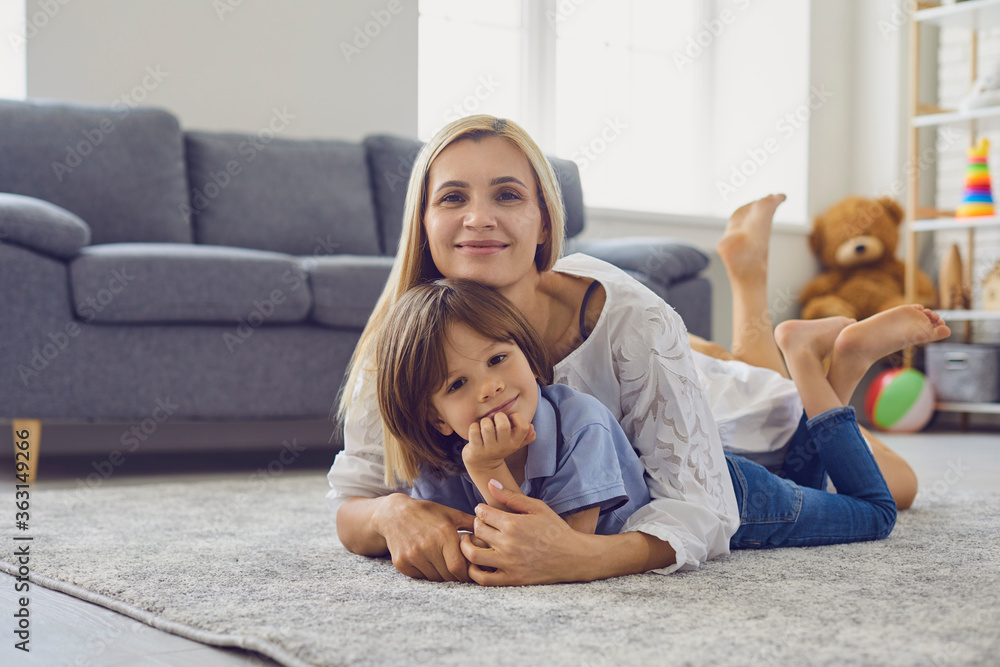 Loving mother hugging her son while lying on carpet in living room. Parent and child embracing at home. Family bonding Loving mother hugging her son while lying on carpet in living room. Parent and child embracing at home. Family bonding