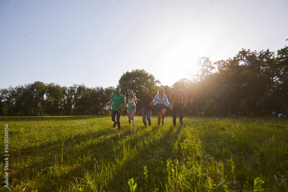 Group of happy young people running on grass in summer park. Youth on vacation. Group of happy young people running on grass in summer park. Youth on vacation.