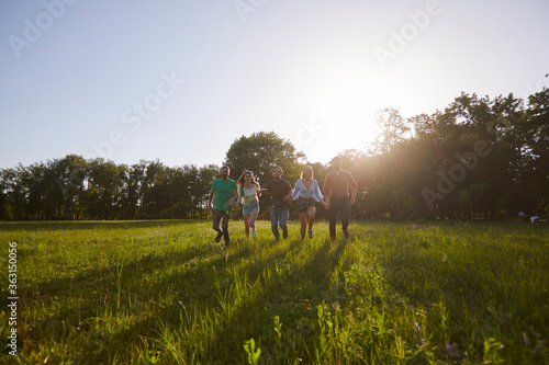Group of happy young people running on grass in summer park. Youth on vacation.