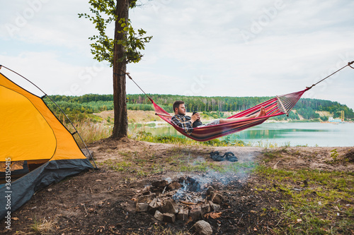 man laying on hammock at lake beach near camp fire