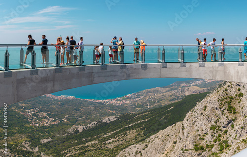 Tourists walking accross the newly built skywalk on Biokovo mountain. Wide view from the entrance, towns and the sea visible in far distance photo
