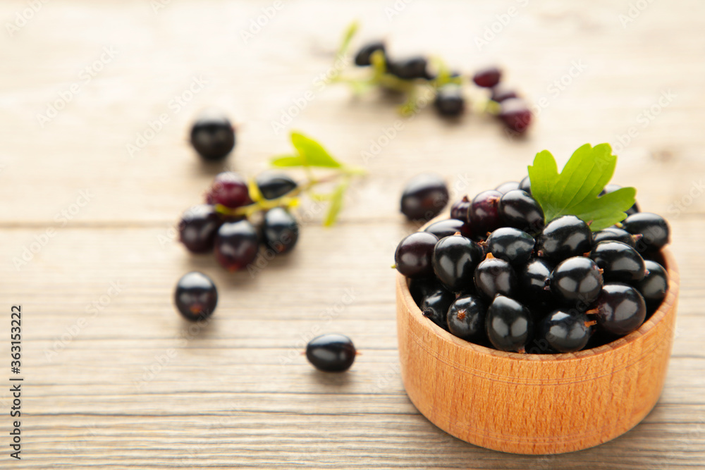 Black currant with leaf in wooden bowl on grey wooden table Black currant with leaf in wooden bowl on grey wooden table