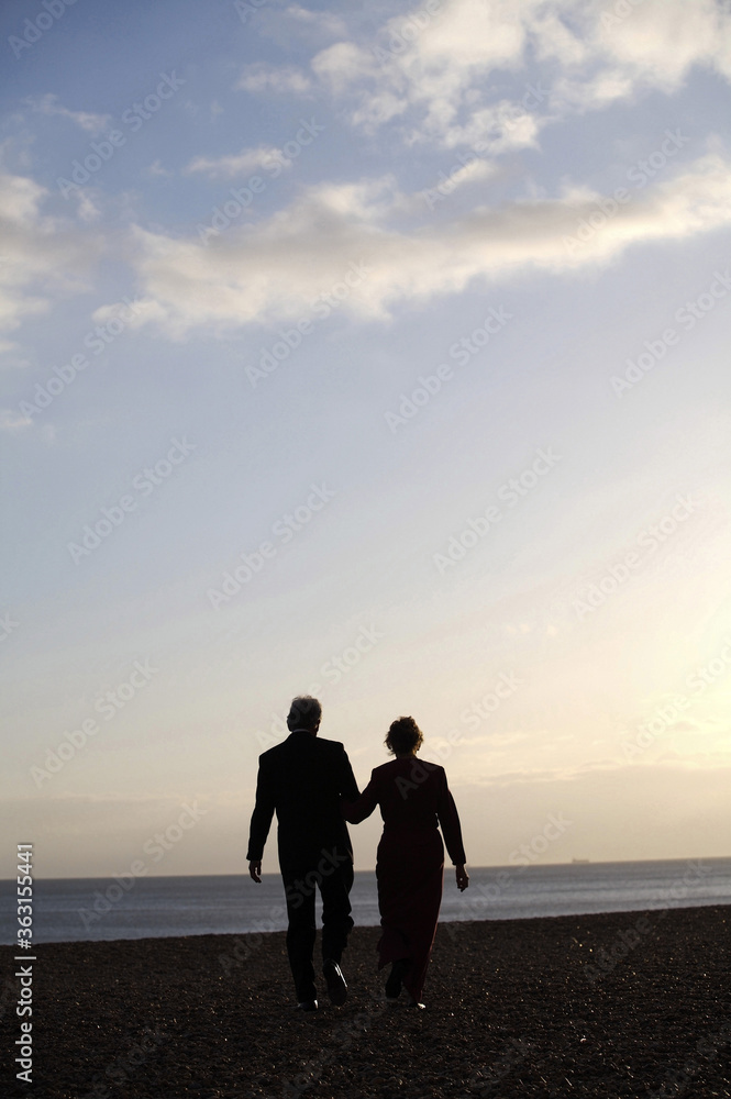 A couple walking hand-in-hand on the beach in the evening