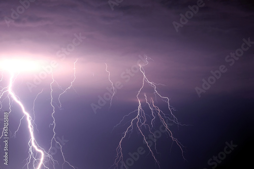 Many bright lightning discharges in the stormy sky under heavy purple rain clouds