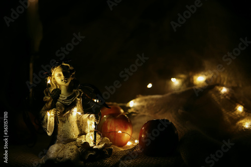 sculpture of a sitting angel against a burning candle and yellow garlands in the dark