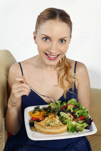 Woman holding a plate of quiche with garden salad and fresh herbs
