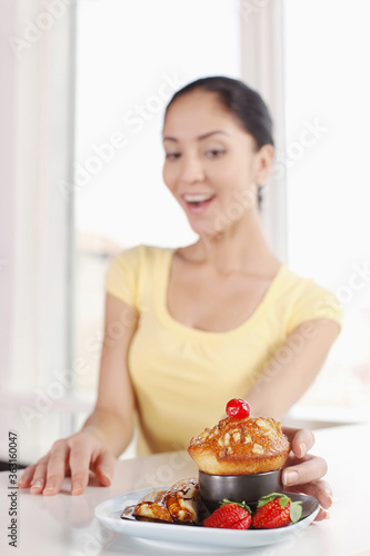 Woman looking at pecan muffin served with fruits and chocolate sauce