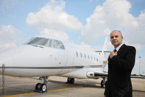 Businessman adjusting his tie on runway with private jet in the background