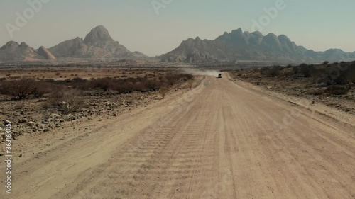 Aerial view of a 4x4 4WD car cruising the desert with Skitzkoppe moutain in the background, surrounded by savanna flatlands, must-see destination in Namibia