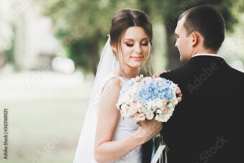 Stylish couple of happy newlyweds walking in the park on their wedding day with bouquet