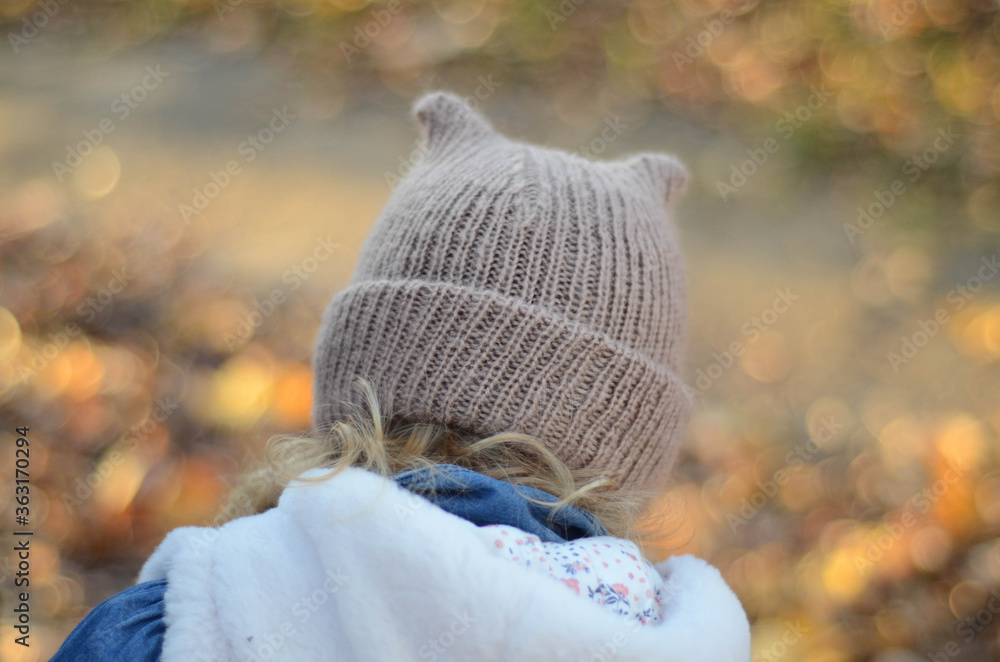 Picture of a smiling blonde toddler girl playing outside in the funny knitted hat with cat ears Picture of a smiling blonde toddler girl playing outside in the funny knitted hat with cat ears