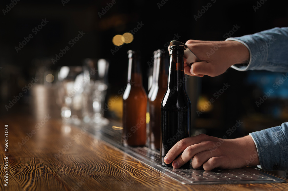 Evening with company in pub. Barman opens beer bottles on wooden bar counter