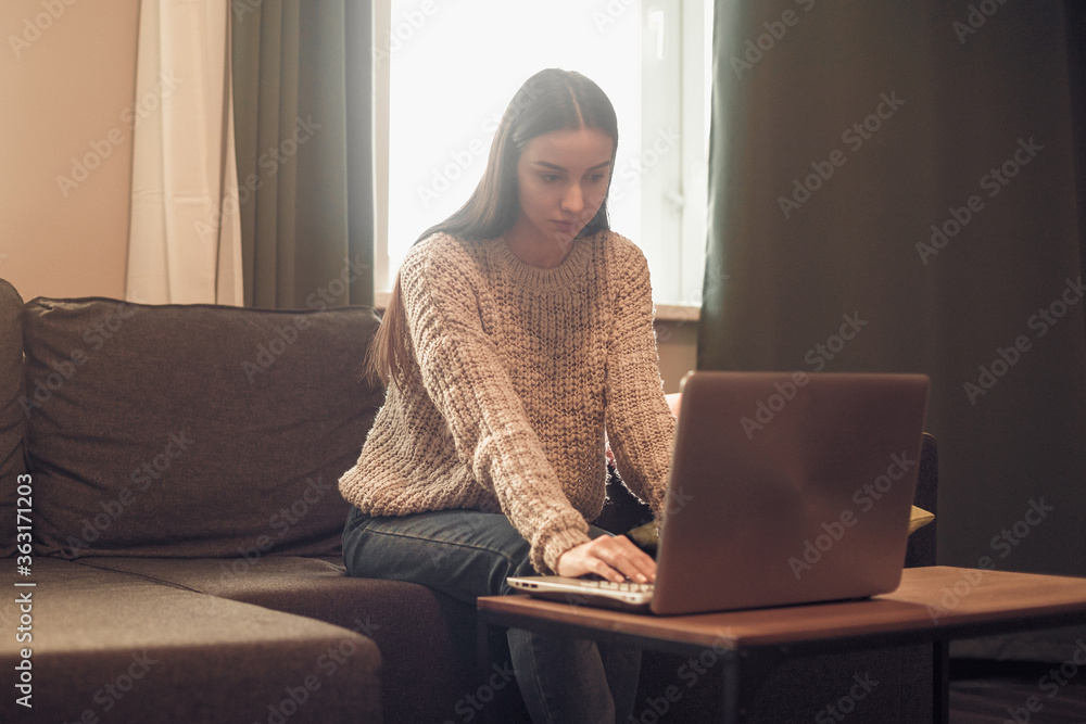 Young woman with modern laptop sitting on sofa at home Young woman with modern laptop sitting on sofa at home