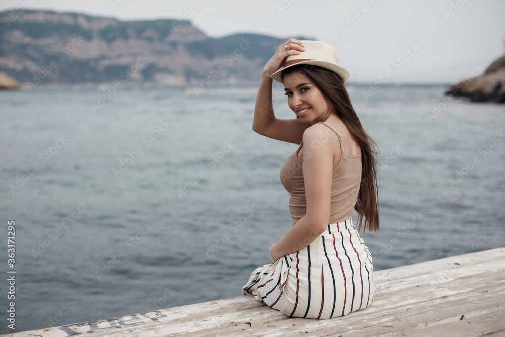 Back side young smiling happy woman sitting near sea on a pier