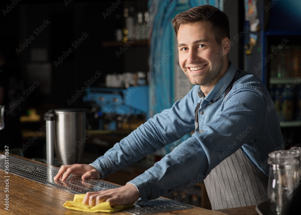 Friendly client meeting. Smiling man in apron, wipes bar counter Friendly client meeting. Smiling man in apron, wipes bar counter