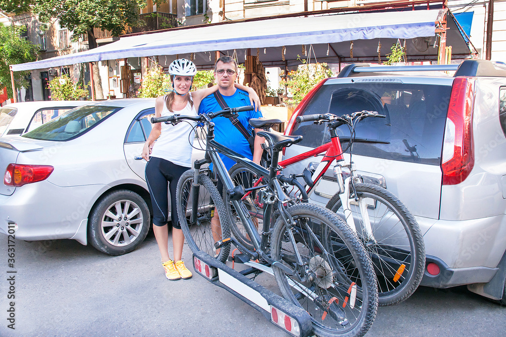 Man and woman are standing near two bicycles mounted on trunk of car.