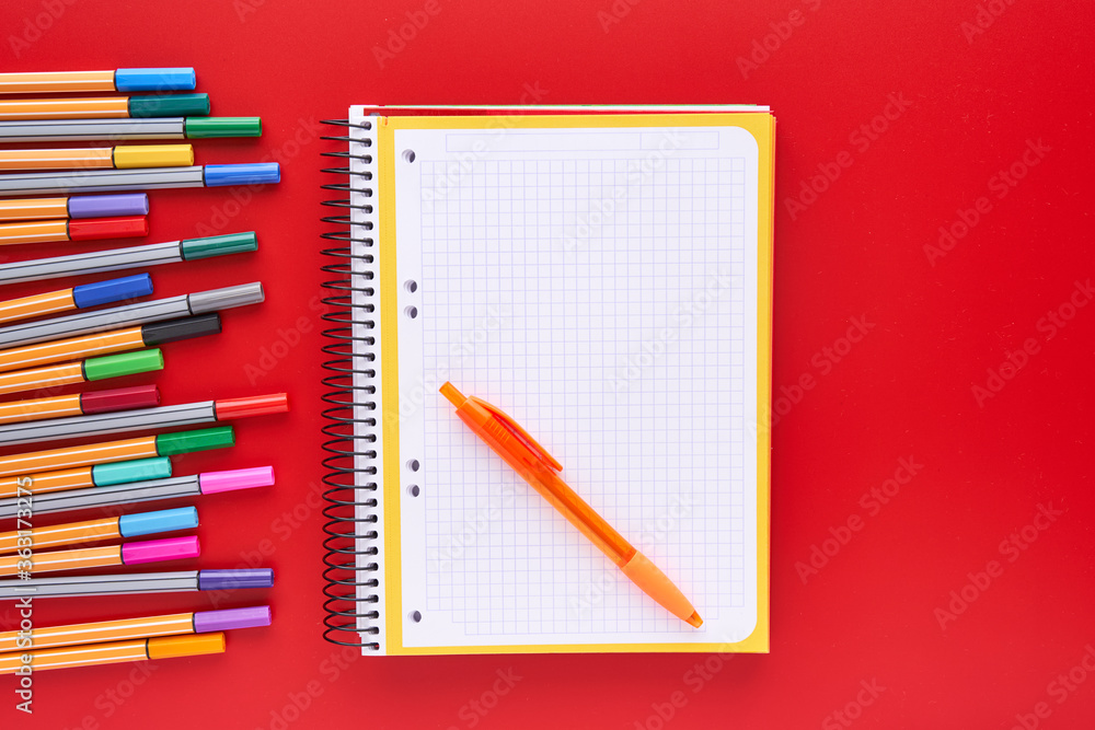 Coloured markers and a notebook on a red background. Back to school concept and crafts. Coloured markers and a notebook on a red background. Back to school concept and crafts.