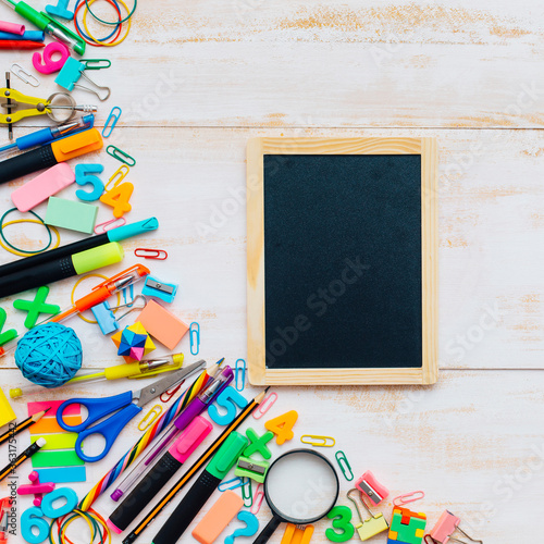 Blank small chalkboard with group of school supplies on a white wooden background.
