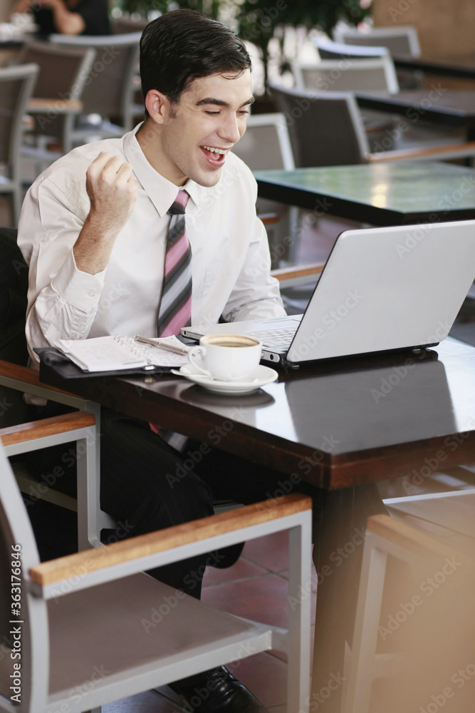 Businessman cheering while using laptop