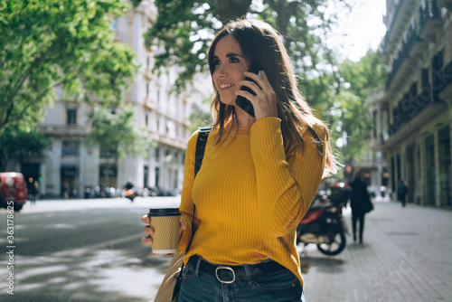 Lifestyle portrait of happy woman walking in the city on a sunny summer day, beautiful young girl dressed in casual style talking on smartphone device, flare light.
