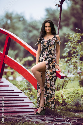A beautiful girl stands near a decorative motive in the park. Beautiful brunette on a background of blurred nature. Sexy young girl in a long dress. Everyday life of a beautiful young lady.
