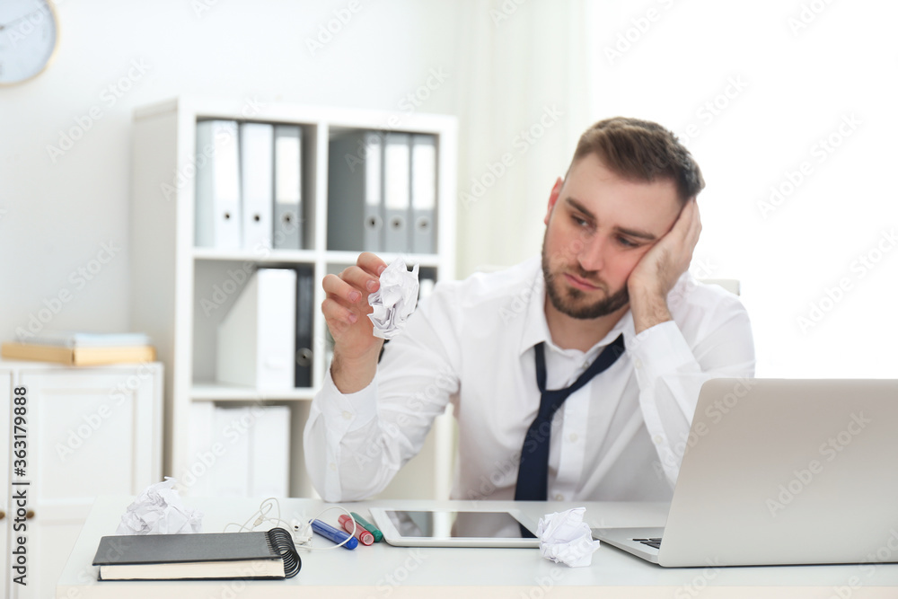 Lazy young man with crumpled paper at messy table in office, focus on hand
