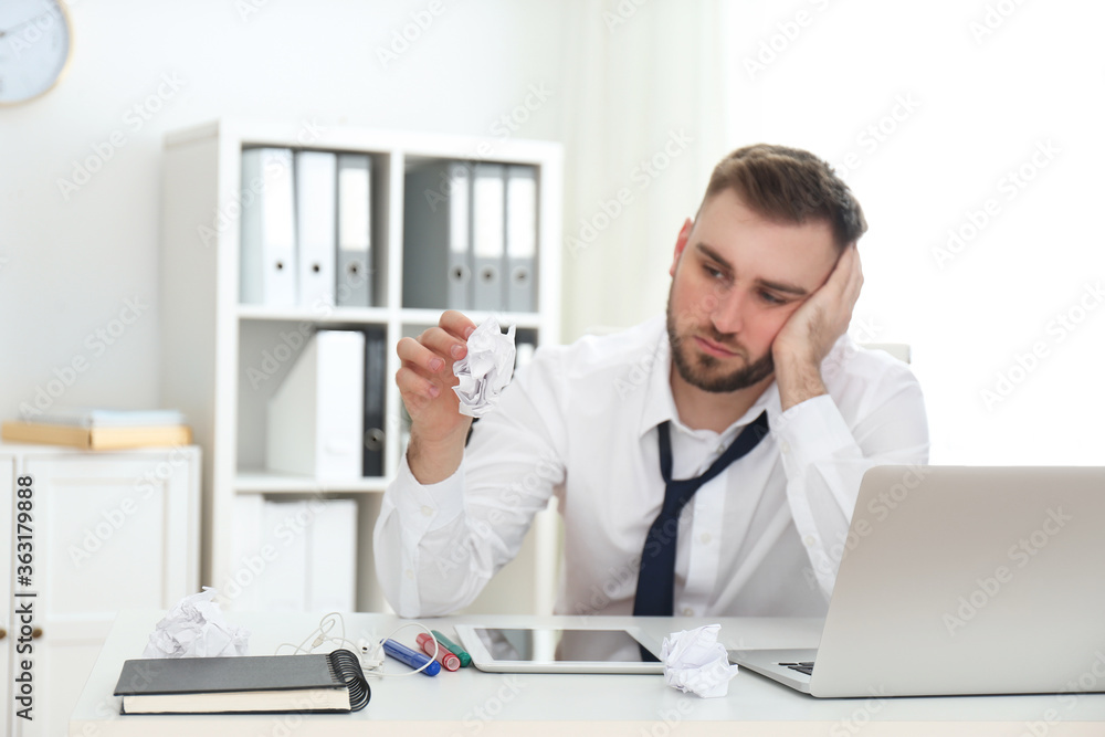 Lazy young man with crumpled paper at messy table in office, focus on hand Lazy young man with crumpled paper at messy table in office, focus on hand