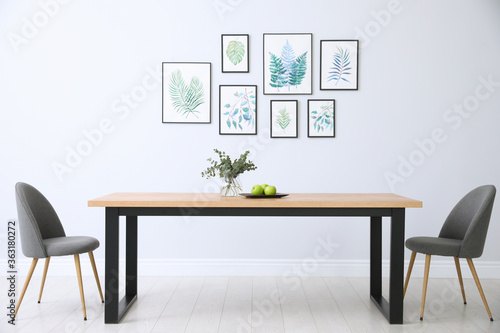 Fototapeta Naklejka Na Ścianę i Meble -  Stylish room interior with modern table, chairs and paintings of tropical leaves. Idea for design