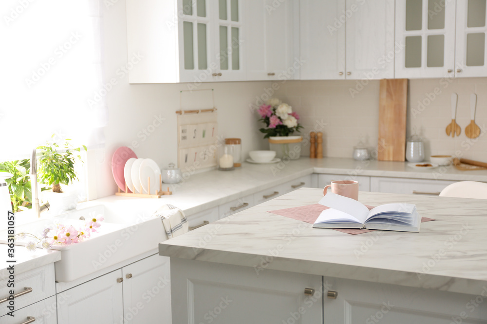 Book and cup on white marble table in modern kitchen. Interior design Book and cup on white marble table in modern kitchen. Interior design
