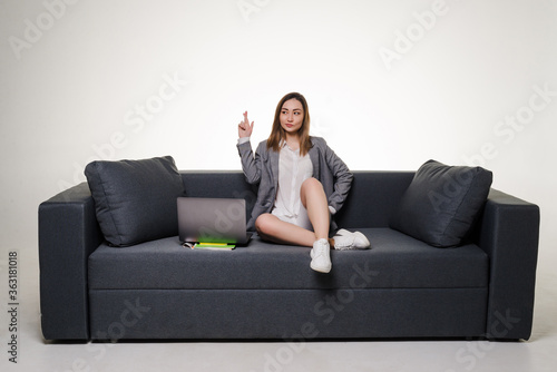 Beautiful asian woman on a sofa working with a laptop with crossed fingers in white background © dianagrytsku