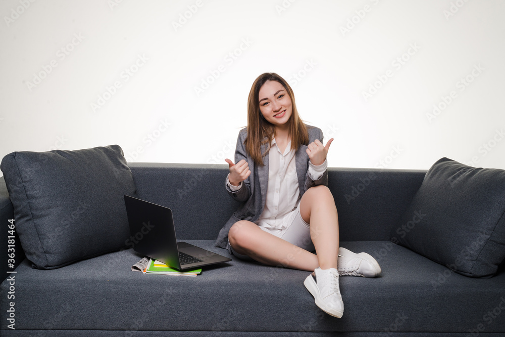 Obraz premium Young woman showing thumb up with laptop on sofa with thumbs up isolated on white