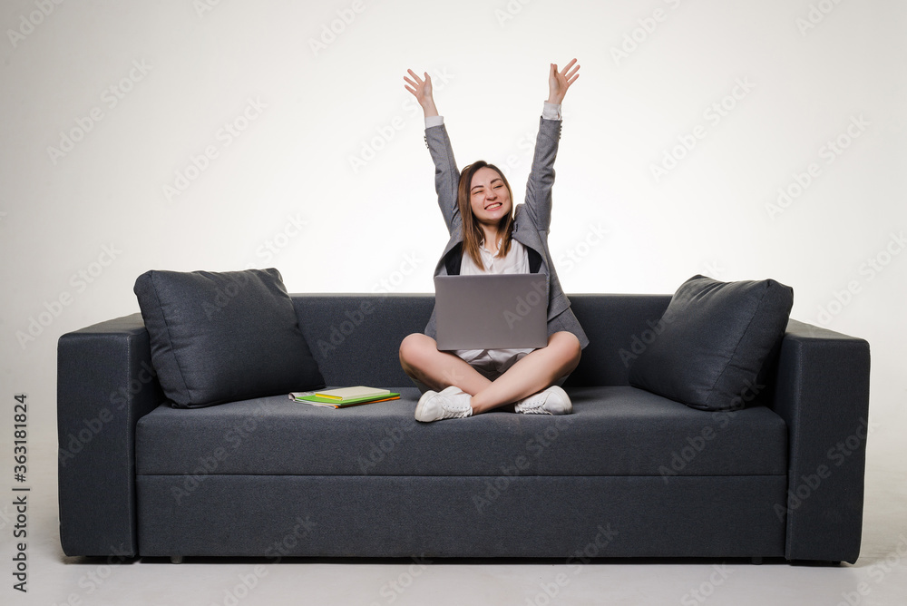 Happy young woman using laptop sitting at sofa isolated on white background