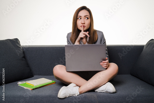 Thoughtful young woman sitting on the couch with laptop, isolated on white background