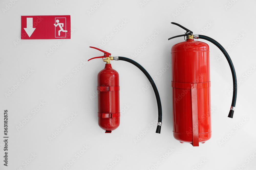 Fire extinguishers and emergency exit sign on white wall