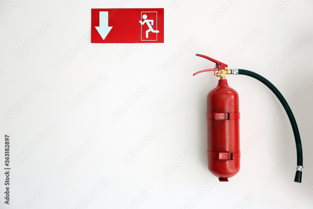 Obraz premium Fire extinguisher and emergency exit sign on white wall, space for text
