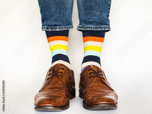 Men s legs  trendy shoes  blue jeans and variegated  long socks on a white  isolated background. Close-up. Concept of style and elegance
