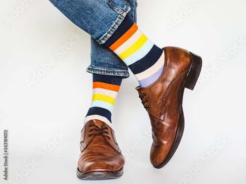 Men's legs, trendy shoes, blue jeans and variegated, long socks on a white, isolated background. Close-up. Concept of style and elegance