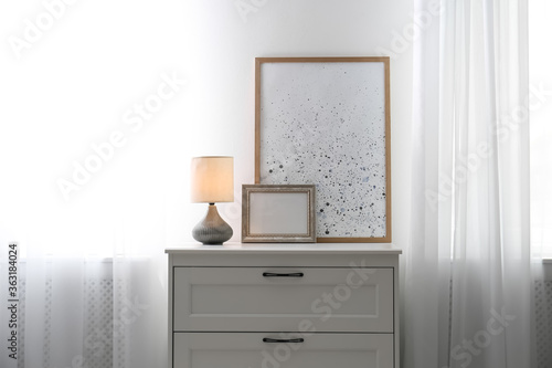 Modern chest of drawers with lamp near window indoors