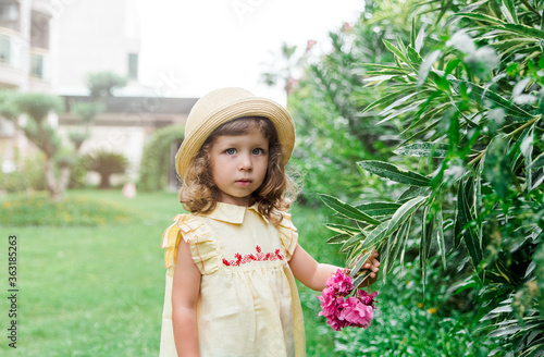 Pretty little girl in a yellow dress and a straw hat in green beautiful garden outdoor