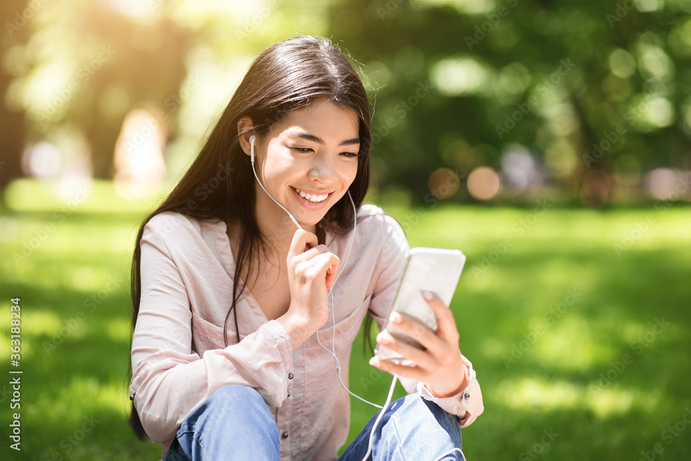 Joyful Korean Girl Having Video Call On Smartphone While Relaxing In Park Joyful Korean Girl Having Video Call On Smartphone While Relaxing In Park