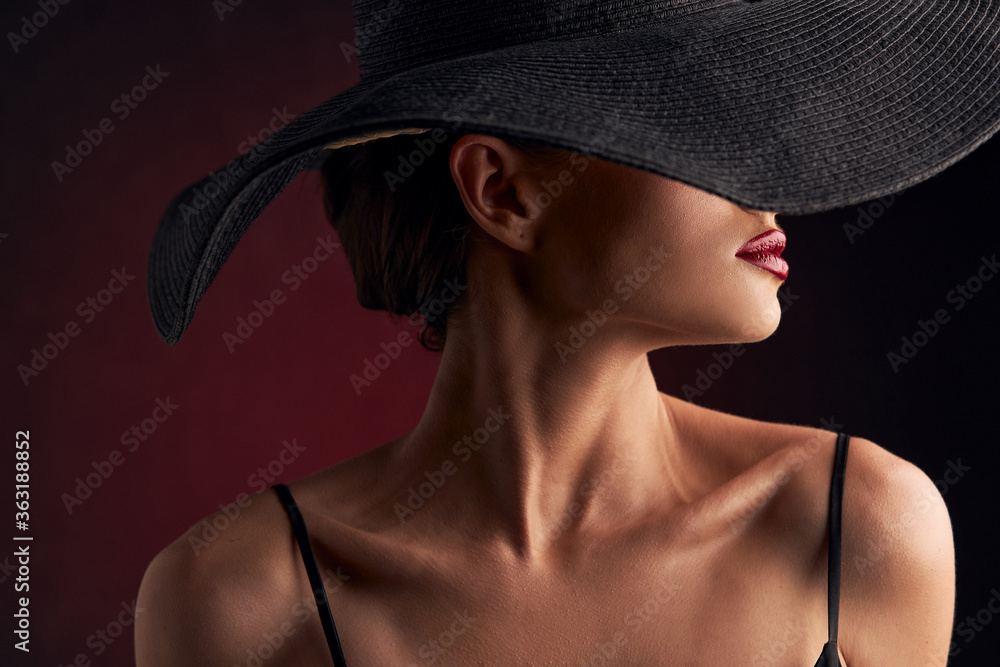 profile portrait of a beautiful tanned girl with professional makeup, red lips on a burgundy background in a black dress with straps, a black hat that covers half of her face profile portrait of a beautiful tanned girl with professional makeup, red lips on a burgundy background in a black dress with straps, a black hat that covers half of her face