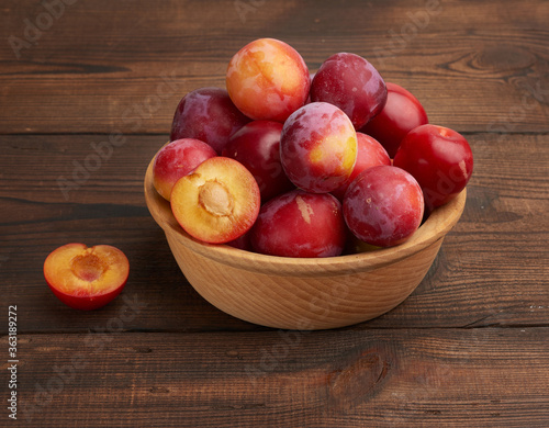 ripe red plums in a round wooden plate on the table