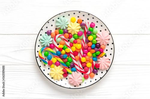 mix colorful sweets - white round plate with black peas, lollipop, meringue, chocolate, sprinkle on wooden background Flat lay Top view Holiday card Happy birthday party concept