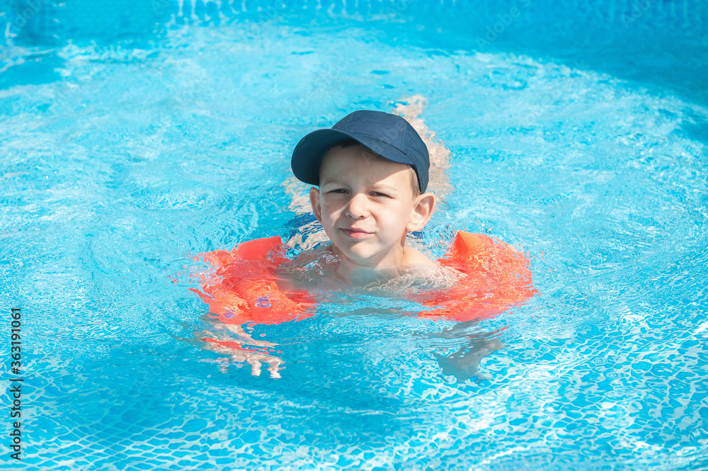 child boy swims in a pool with arm ruffles and a baseball cap. safe swimming